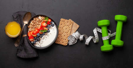 Healthy breakfast with bowl of granola, yogurt and fresh berries. Fitness protein meal. Dumbbells and tape measure. Diet concept. Top view flat layの写真素材