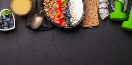 Healthy breakfast with bowl of granola, yogurt and fresh berries. Fitness protein meal. Dumbbells and tape measure. Diet concept. Top view flat lay with copy spaceの写真素材