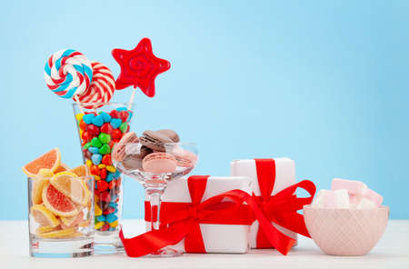 Various sweets assortment. Candy, bonbon, chocolate and macaroons in cocktail glasses and gift boxes over blue background. With copy spaceの写真素材