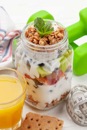 Healthy breakfast with jar of granola, yogurt and fresh berries. Fitness protein meal. Dumbbells and tape measure. Diet conceptの写真素材
