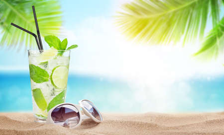 Fresh cold cocktail and sunglasses on tropical beach with palms and bright sand. Summer sea vacation and travel concept with copy spaceの写真素材
