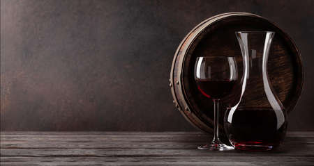 Wine decanter, glass of red wine and old wooden barrel. With copy space