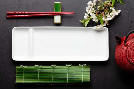 Japanese food plate, cherry blossom, teapot and sushi chopsticks. Top view flat lay with copy space...