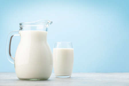 Milk in glass and jug in front of blue background with copy spaceの写真素材