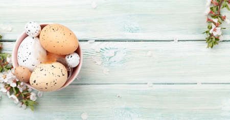Easter eggs in bowl and cherry blossom over blue wood. Spring greeting card with copy space. Top...