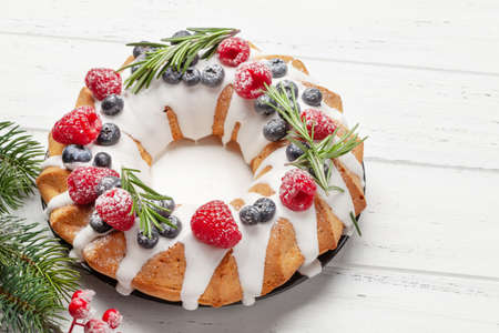 Christmas cake with berries and fir tree on wooden table