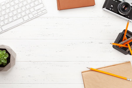 Office desk with supplies, photo camera and potted plant over white wooden table. Top view flat lay with copy spaceの写真素材
