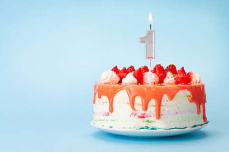 Birthday cake with number one candle on a blue background with copy space for your greetings
