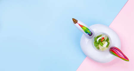 Mojito cocktail in inflatable unicorn toy on blue and pink background. Holiday and vacation. Top...