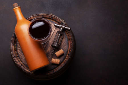 Wine bottle, vintage corkscrew and red wine glass on old wooden barrel. Top view flat lay with copy...