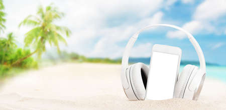 Smartphone and headphones on tropical sea beach with palms and bright sand. Summer sea vacation, music and travel concept. With white screen for your appの写真素材