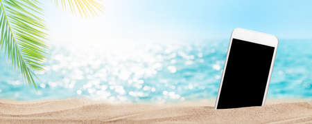 Smartphone on tropical sea beach with palms and bright sand. Summer sea vacation, music and travel concept. With blank screen for your appの写真素材