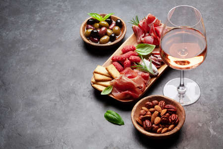 Antipasto board with prosciutto, salami, crackers, cheese, nuts, olives and rose wine. With copy spaceの写真素材