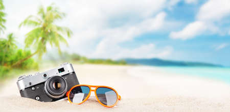 Retro camera and sunglasses on tropical beach with palm leaves and bright sand. Summer sea vacation and travel concept with copy spaceの写真素材