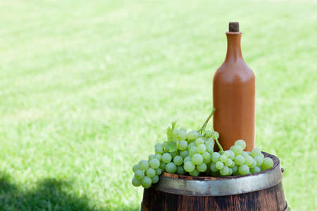 Grapes and wine bottle on wine barrel on outdoor sunny garden with copy space