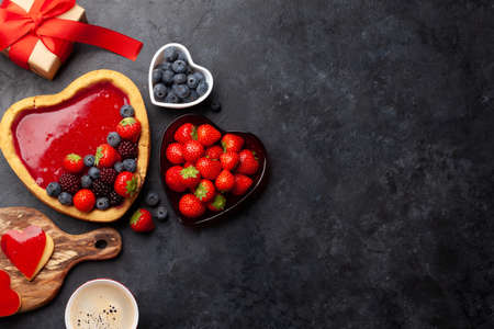 Heart shaped sweet cake with berries, coffee and gift box. Valentines Day greeting card. Top view flat lay with copy spaceの写真素材