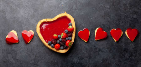 Heart shaped sweet cake with berries and cookies. Valentines Day greeting card. Top view flat lay with copy spaceの写真素材