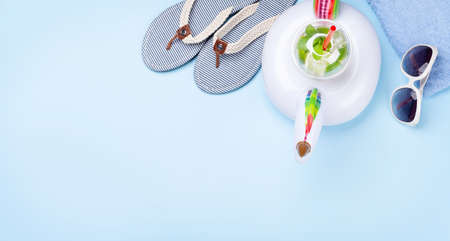 Travel and vacation items on blue background. Sunglasses, cocktail, flip flops and inflatable. Top...