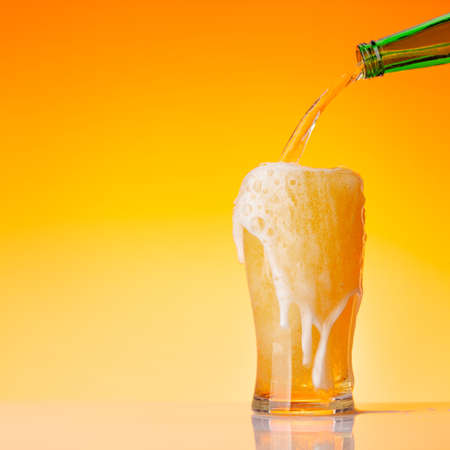 Beer pouring from bottle into glass in front of yellow background. Studio shot with copy spaceの写真素材