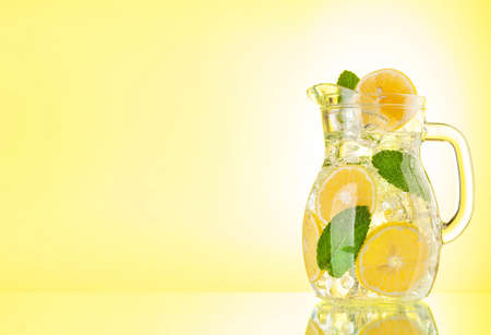 Lemonade pitcher with lemon, mint and ice cubes. Over yellow background with copy space