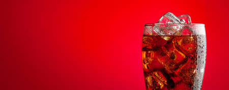 Cola with ice. Fresh cold sweet drink with ice cubes. Over red background with copy spaceの写真素材