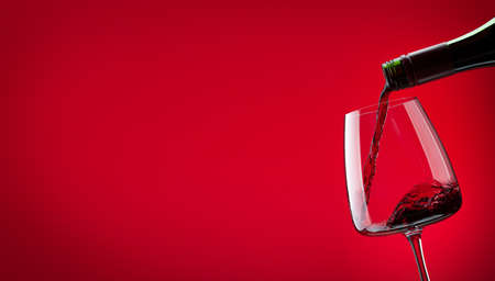 Red wine pouring from bottle into glass over red background with copy spaceの写真素材