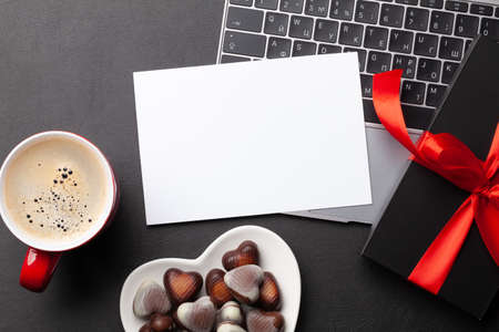 Gift box and chocolate heart sweets over laptop on office desk table. Top view flat lay with blank greeting card for your greetings. Valentines day templateの写真素材