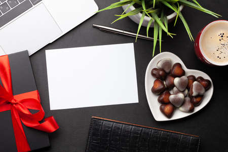 Gift box and chocolate heart sweets over laptop on office desk table. Top view flat lay with blank...