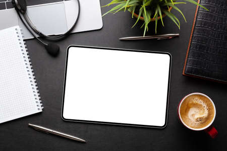 Tablet with blank screen on desk, coffee cup and office supplies. Top view flat lay with copy space