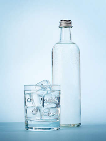 Water bottle and glass with water and ice cubes over blue background