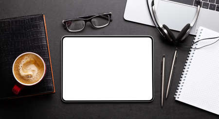 Tablet with blank screen on desk, coffee cup and office supplies. Top view flat lay with copy space