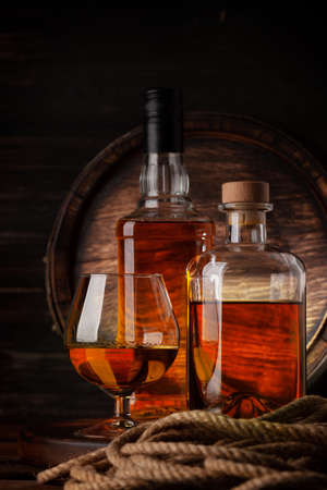 Glass and bottles with cognac, whiskey or golden rum. In front of old wooden barrelの写真素材