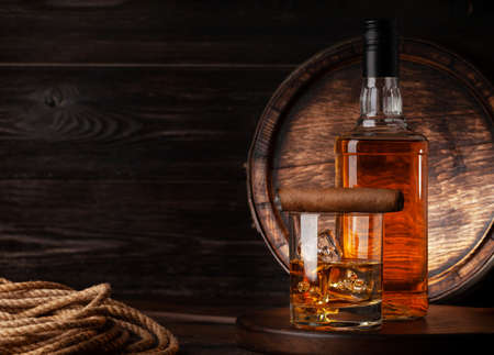Glass and bottle with cognac, whiskey or golden rum and cigar. In front of old wooden barrel with copy spaceの写真素材