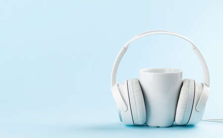 White headphones and cup of coffee over blue background with copy space. Podcast, audiobook or music templateの写真素材