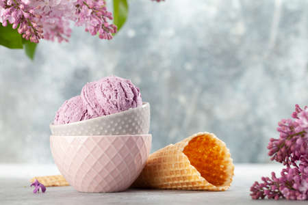 Ice cream sundae in bowl, waffle cones and lilac flowersの写真素材
