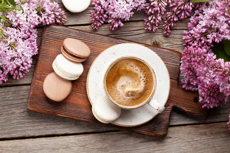 Macaroon cookies and coffee. On wooden table with lilac flowers. Top view flat layの写真素材