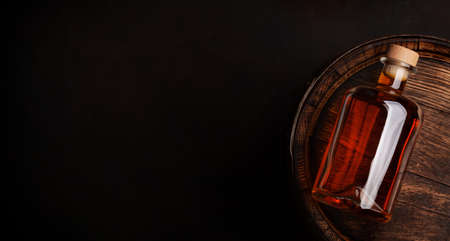 Bottle with rum, cognac or whiskey. Over old wooden barrel. Top view flat lay with copy space