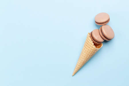 Various macaroon cookies in ice cream cones. Flat lay on blue background with copy spaceの写真素材