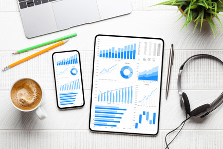 Tablet and smartphone with business reports and charts on desk. Top view flat lay
