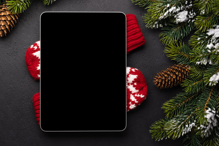 Tablet with blank screen over winter mittens and Christmas decor. Xmas device screen template