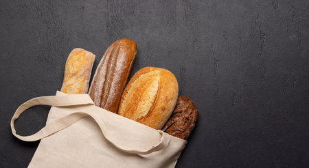 Fresh baked bread in bag on stone table. Flat lay with copy space