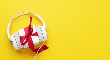 Headphones and gift box on yellow background. Flat lay with copy spaceの写真素材