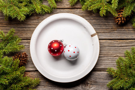 Table setting from above with baubles on plate, Christmas Fir tree branches and pine cones on wooden background. flat layの写真素材