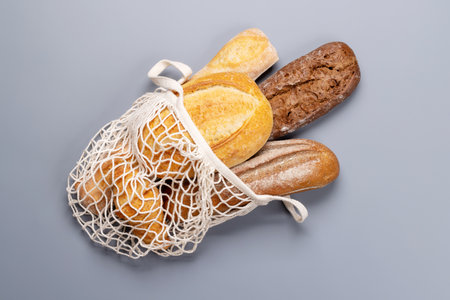 Fresh baked bread in mesh bag on gray background. Flat lay with copy spaceの写真素材