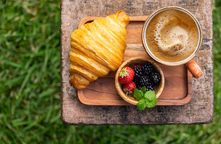 Coffee cup and croissant on outside garden table. Sunny outdoor meal. flat layの写真素材