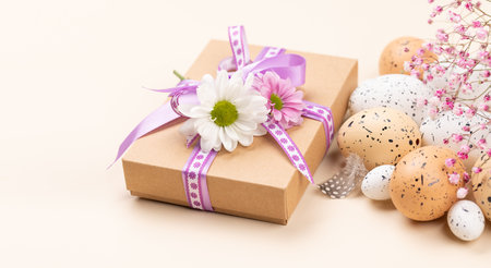 Gift box, Easter eggs and flowers on a beige background with space for your greetings