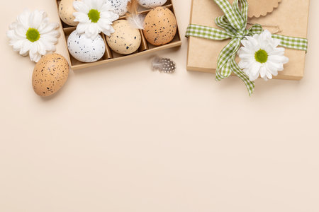 Gift box, Easter eggs and flowers on a beige background with space for your greetings. flat lay