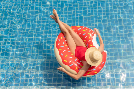 Beautiful young woman with inflatable donut ring relaxing in swimming pool. summer holidays. top view with copy spaceの写真素材