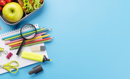 School supplies, stationery, and lunch box on blue background. education and nutrition. Flat lay...