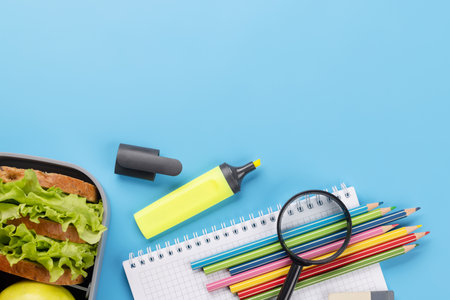 School supplies, stationery, and lunch box on blue background. education and nutrition. Flat lay with blank spaceの写真素材